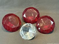 Three ruby red and one clear faceted glass paperweights grouped