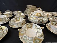 Assorted cups, double-handled soup bowls, saucers and covered dish showing pattern and gilt trimming
