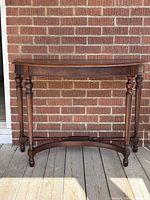 Front view of mahogany demilune console table against brick wall