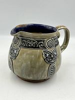 Front view of Royal Doulton pitcher showing Maori masks and scroll band