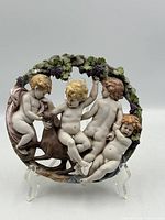 Front view of round porcelain plaque showing four cherubs, dog, grapevine wreath
