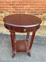 Full view of round wooden side table showing drawer, legs, and lower shelf