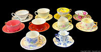 Overhead view of all ten demitasse cup and saucer sets on black background