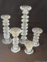 Front view of all five clear glass candlesticks showing graduated heights and texture