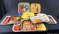 Group view of all 12 metal whisky advertising trays, various brands visible