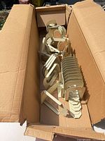 Open carton containing stacked beige metal L-shaped brackets