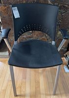 Front view of black plastic office chair with metal frame and armrests