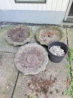 Three concrete bird bath basins on patio next to bucket