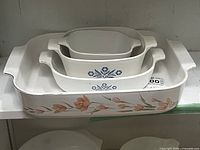 Stacked view showing all four dishes: outer peach tulip roaster and three nested Blue Cornflower casseroles