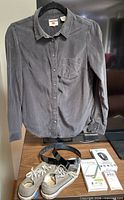 Front view of gray Levi's shirt on hanger with sneakers, belt, power bank, fitness band on table