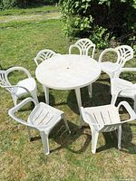 Round white plastic patio table with six matching chairs on lawn