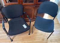 Both black stacking chairs side by side on hardwood floor