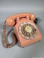 Front three-quarter view showing entire pink rotary telephone and coiled cord
