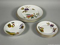 Stacked dinner plates, dessert plates and bowl showing fruit motifs and gold rims