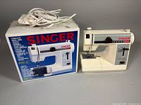 Sewing machine beside original box with power cord visible