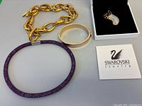 Group shot of all four jewelry items including brooch in box, chain necklace, bangle, and choker