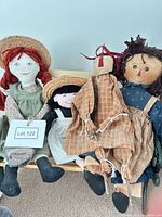 Group shot of four handmade cloth dolls seated on bench