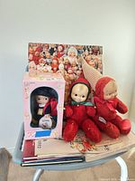 Group view showing boxed Kewpie doll, two red plush elf dolls, poster and paper items