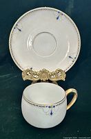 Front view of teacup placed before saucer showing pattern and gold handle