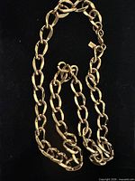 Full view of gold-tone Monet link necklace coiled on black background