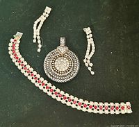 Bracelet, earrings and pendant laid out on dark background