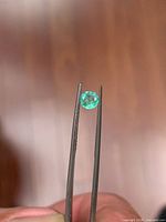 Emerald held in tweezers, showing face-up green color