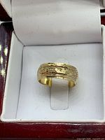close front view of gold-tone engraved ring in box