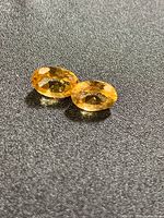 Two oval canary-orange gemstones on dark background showing facets