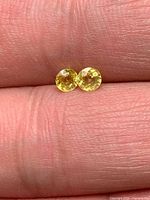 Two yellow round sapphires on fingertip for scale