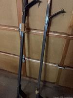 Pair of long black metal roof rack bars leaning against wall