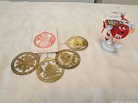 Group shot showing four gold ornaments, packaging card and M&M figurine