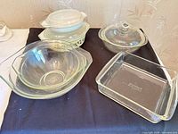 Group shot of all dishes: two clear mixing bowls, round clear casserole with lid, square pan, small white casserole with lid