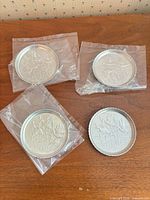 Four aluminum coasters, three in plastic sleeves, one out for view