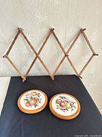 Two round ceramic trivets and wooden expandable wall rack displayed together