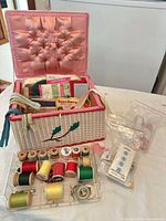 Open wicker sewing basket showing contents: thread spools tray, zippers, bags of notions