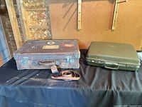 Both suitcases on table, brown W.E. Jackson & Son left, green Samsonite right, strap visible