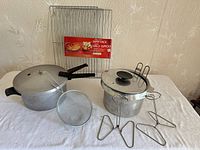 Group shot of all cookware and accessories including pressure cooker, pot with insert, sieve, two poultry stands and wire racks