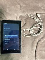 Front view of Amazon Fire 7 tablet turned on next to charging cable