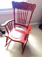 Full view of red wooden rocking chair showing carved back and missing seat