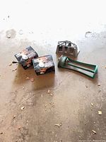 Two boxed NOMA floodlight kits, green oscillating lawn sprinkler, grey hose hanger on concrete floor