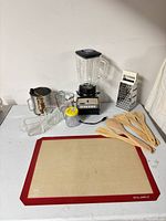 All items laid out on table including blender, utensils, mat, measuring cups, grater, sifter