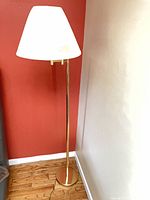 Full view of brass tone floor lamp with white shade in corner