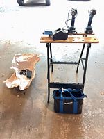 Overall lot showing workbench, two cordless tools, charger, bag and accessories