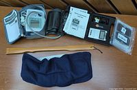 Overview of all items laid out on table: BP monitor kit, TENS unit kit, hot pad, wooden back scratcher