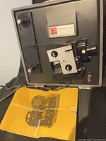 Front view of Kodak Instamatic M60 projector inside carry case with manual visible