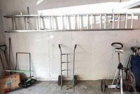 Extension ladder mounted on wall above dolly and other items