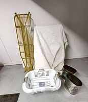 Group view showing ironing board, one laundry basket, covered items, two metal garbage cans