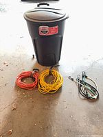 Garbage can, two coiled extension cords, bungee cords on floor