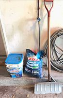 Shovel leaning against wall beside bag and pail of ice melter