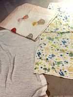 Three bedding pieces laid out: white satin-edged blanket, Sunbonnet Sue quilt, animal print quilt